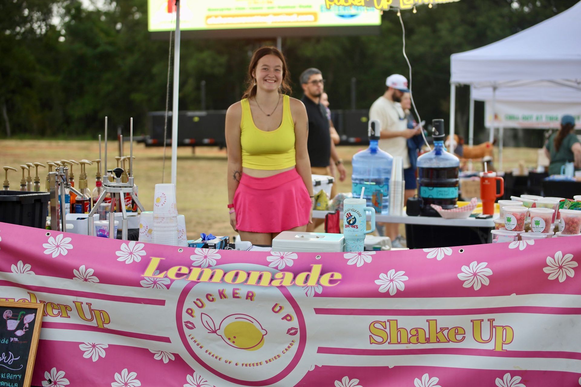 A woman is standing in front of a lemonade stand.