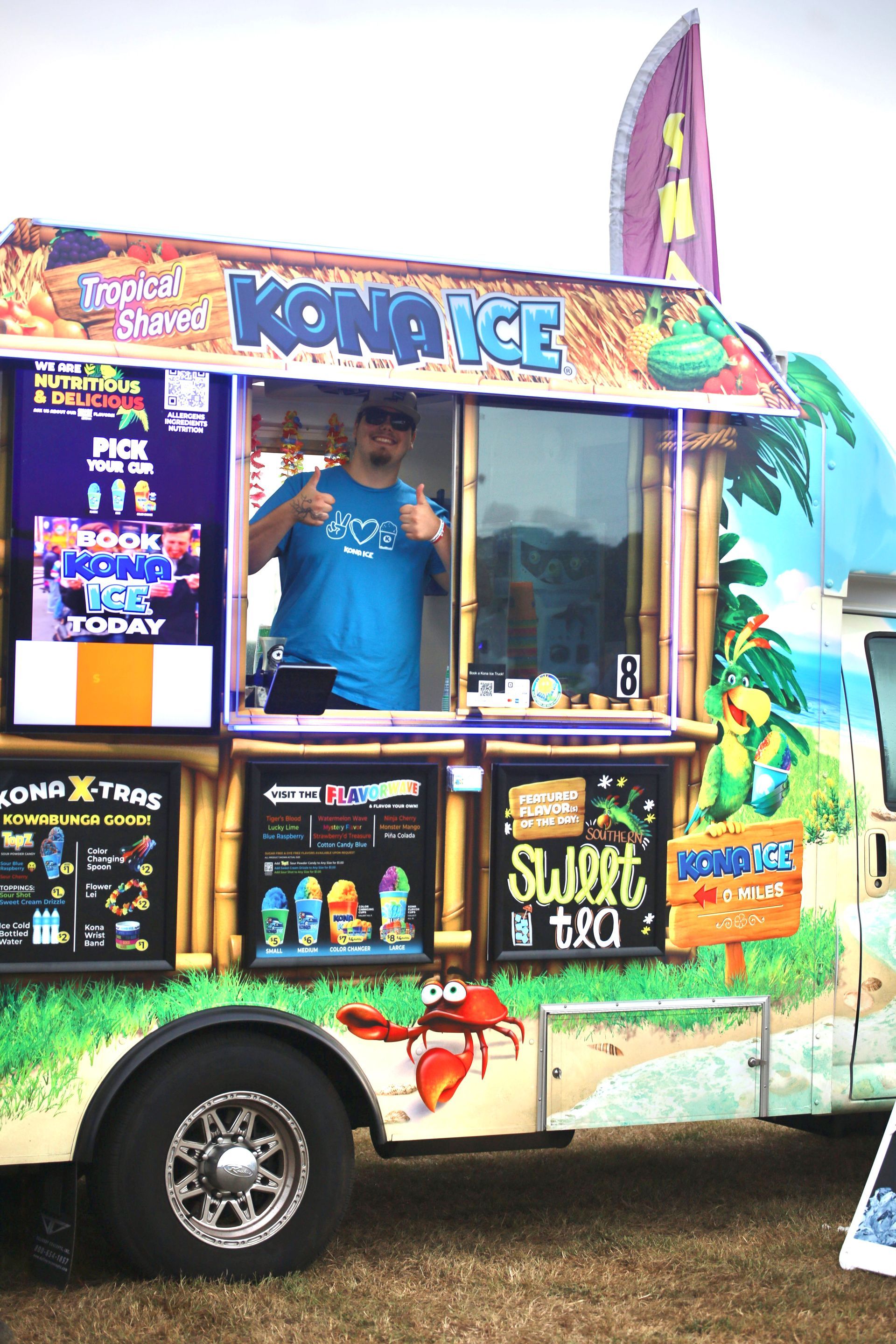 A man is standing in front of a kona ice food truck