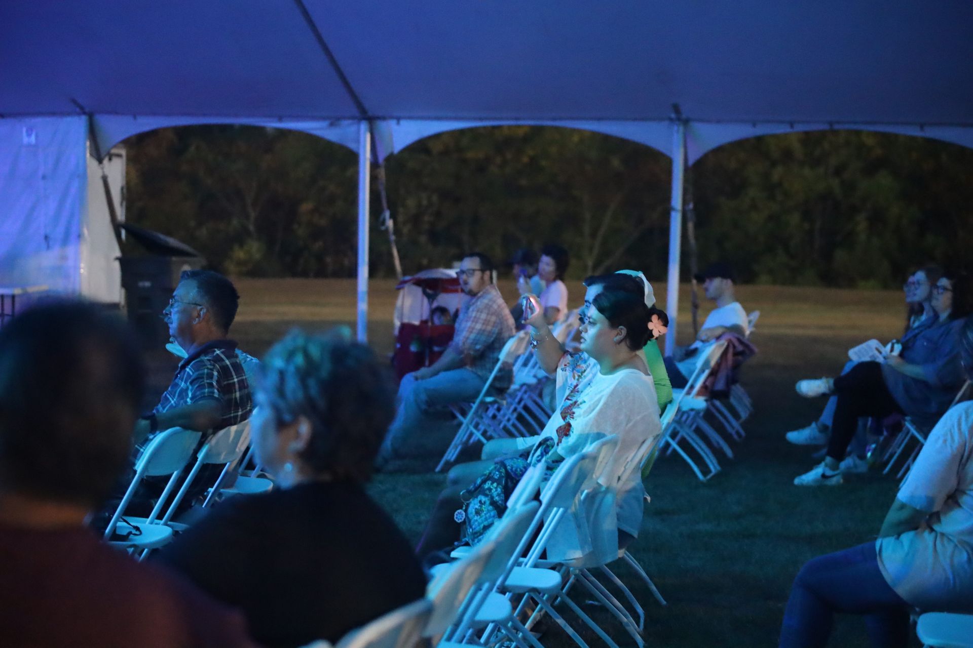 A group of people are sitting in chairs under a tent at night.