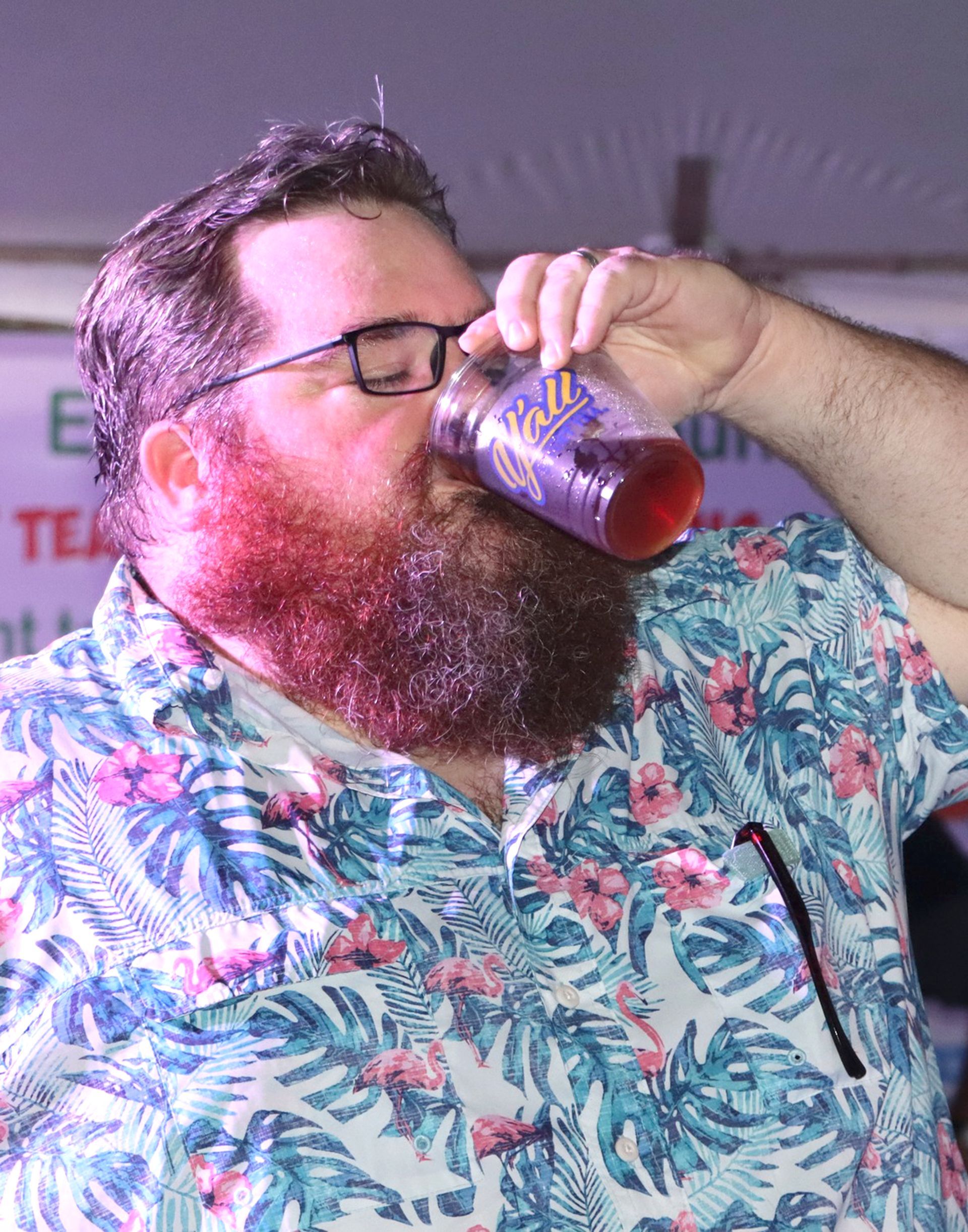 A man with a beard and glasses is drinking from a cup