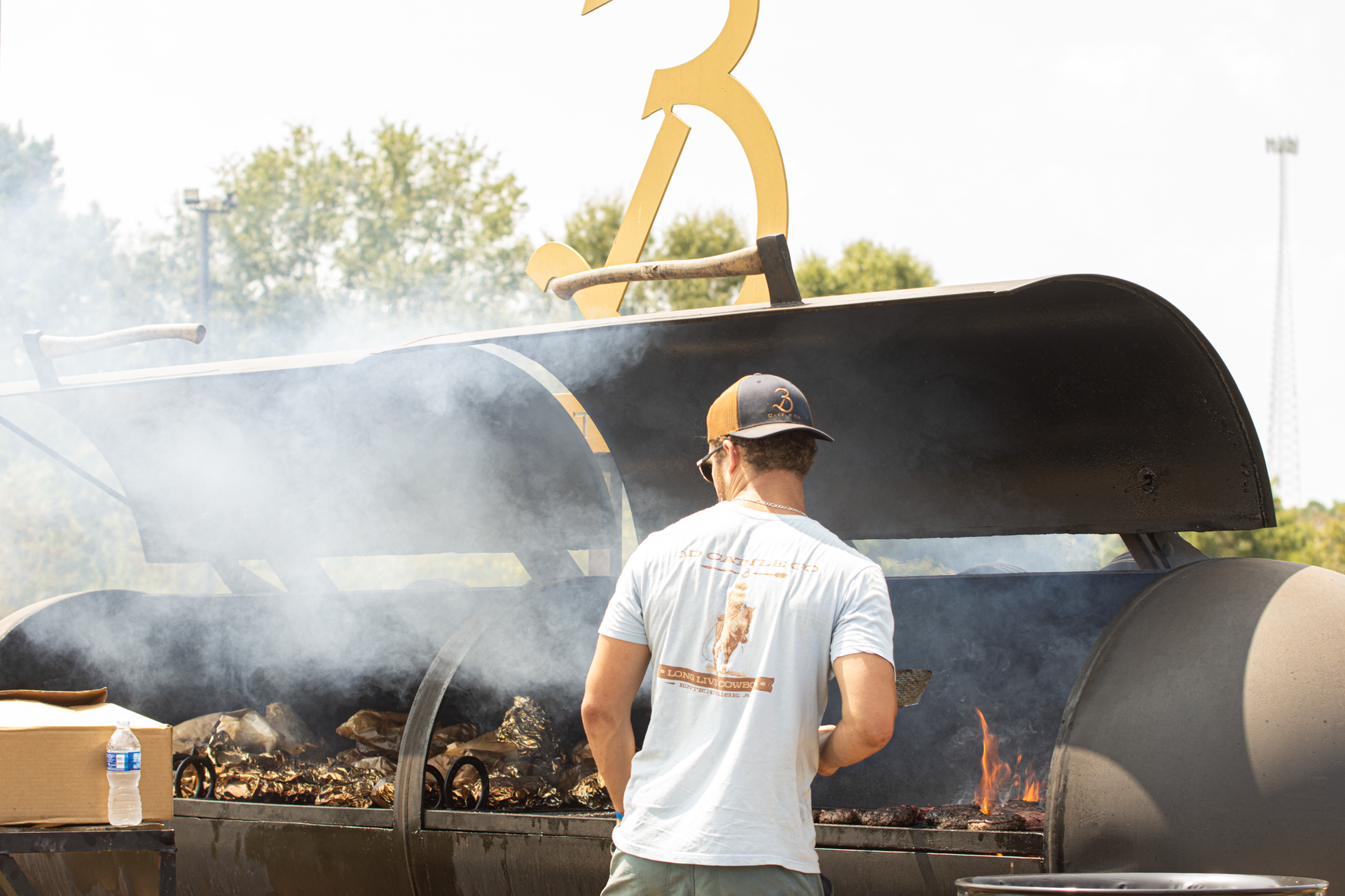 A man in a white shirt is standing in front of a large bbq grill.