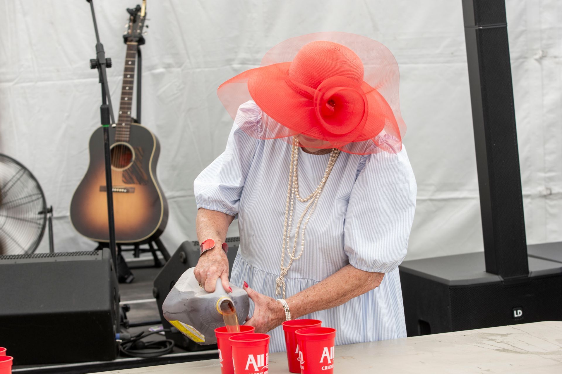 A woman in a red hat is pouring liquid into red cups.