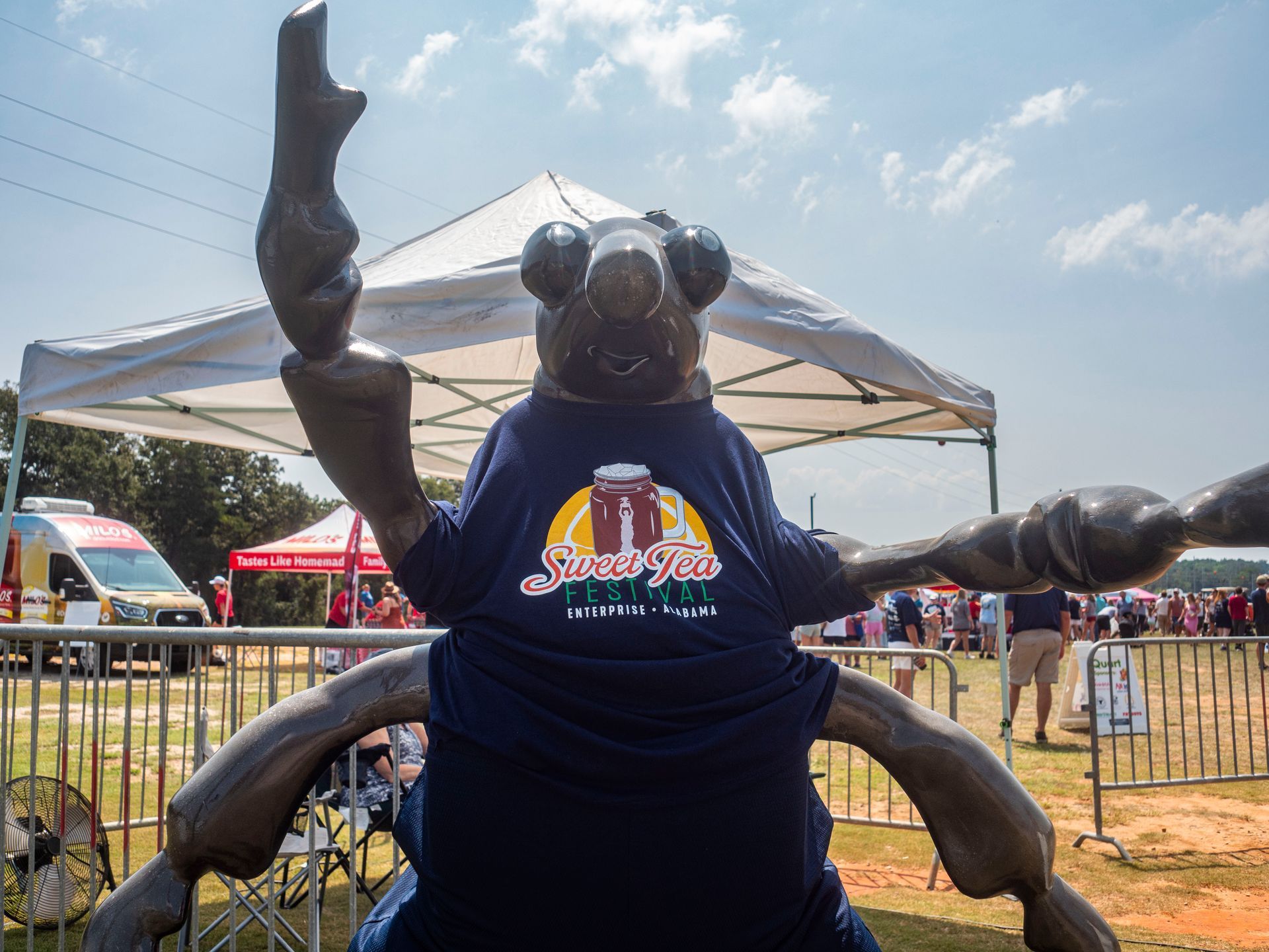 A statue of a bug wearing a blue shirt is standing in front of a tent.