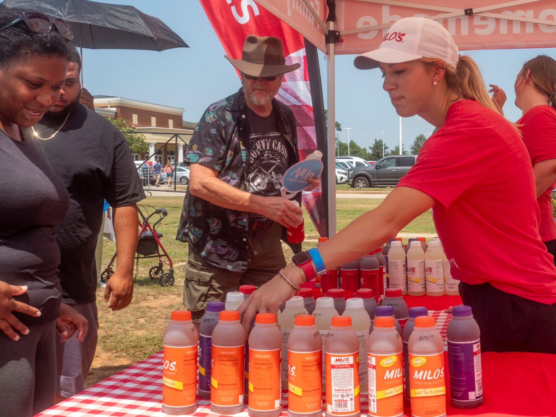 A woman in a red shirt stands behind a table full of bottles of juice