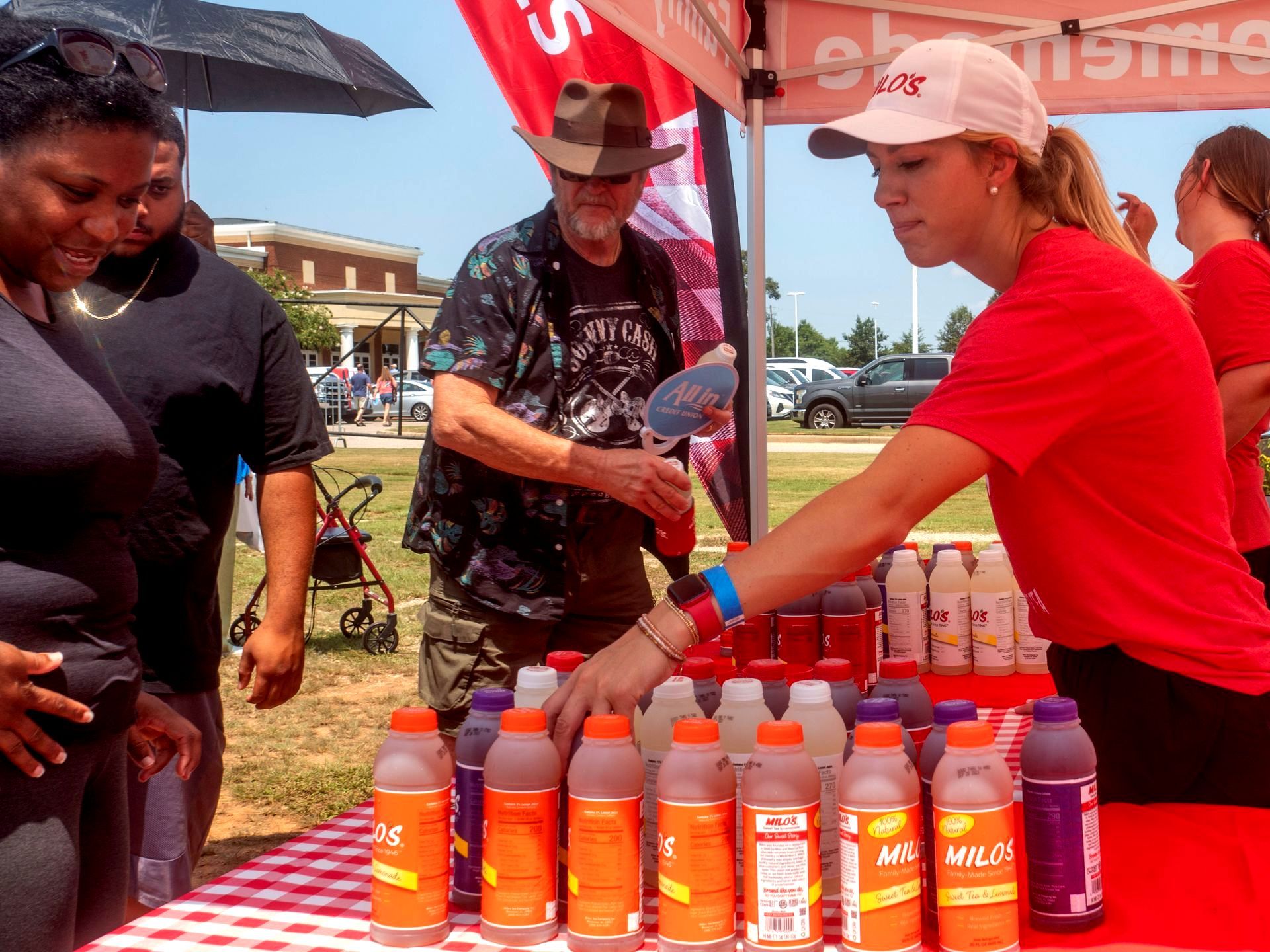 A woman in a red shirt stands behind a table full of bottles of juice