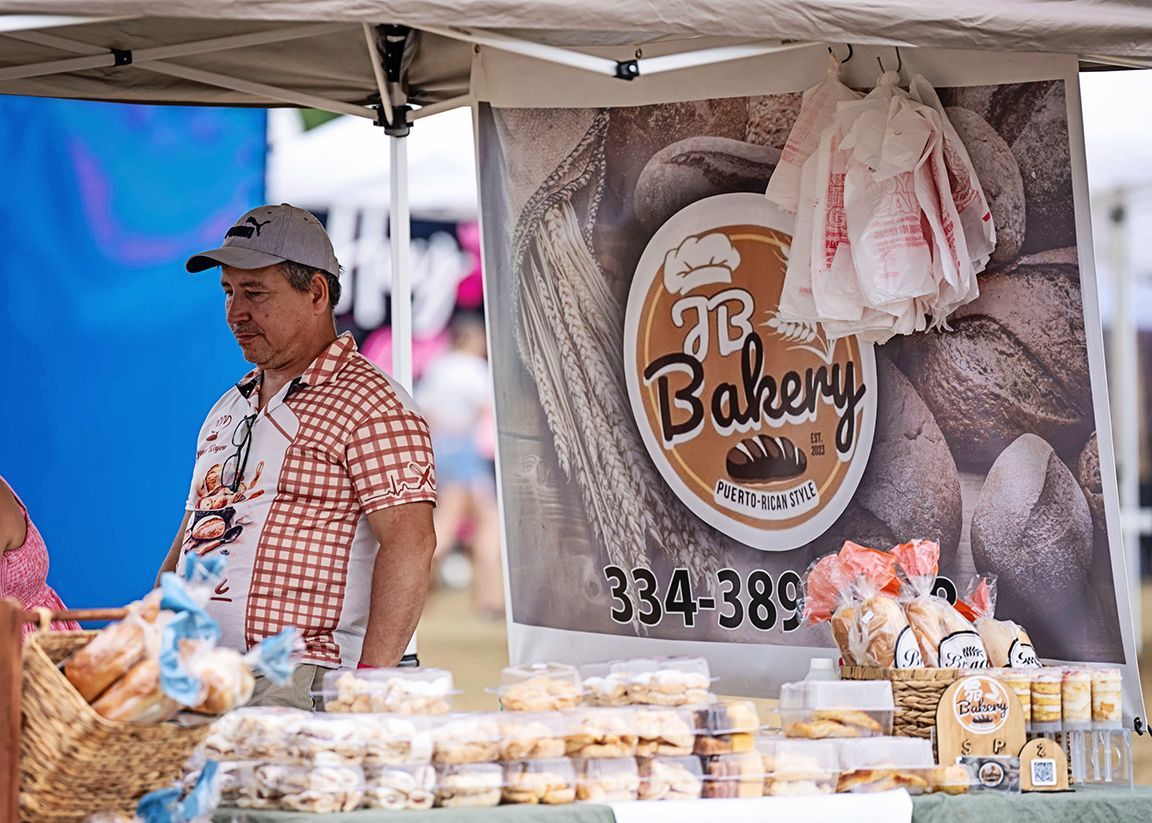 A man is standing behind a bakery stand selling bread.