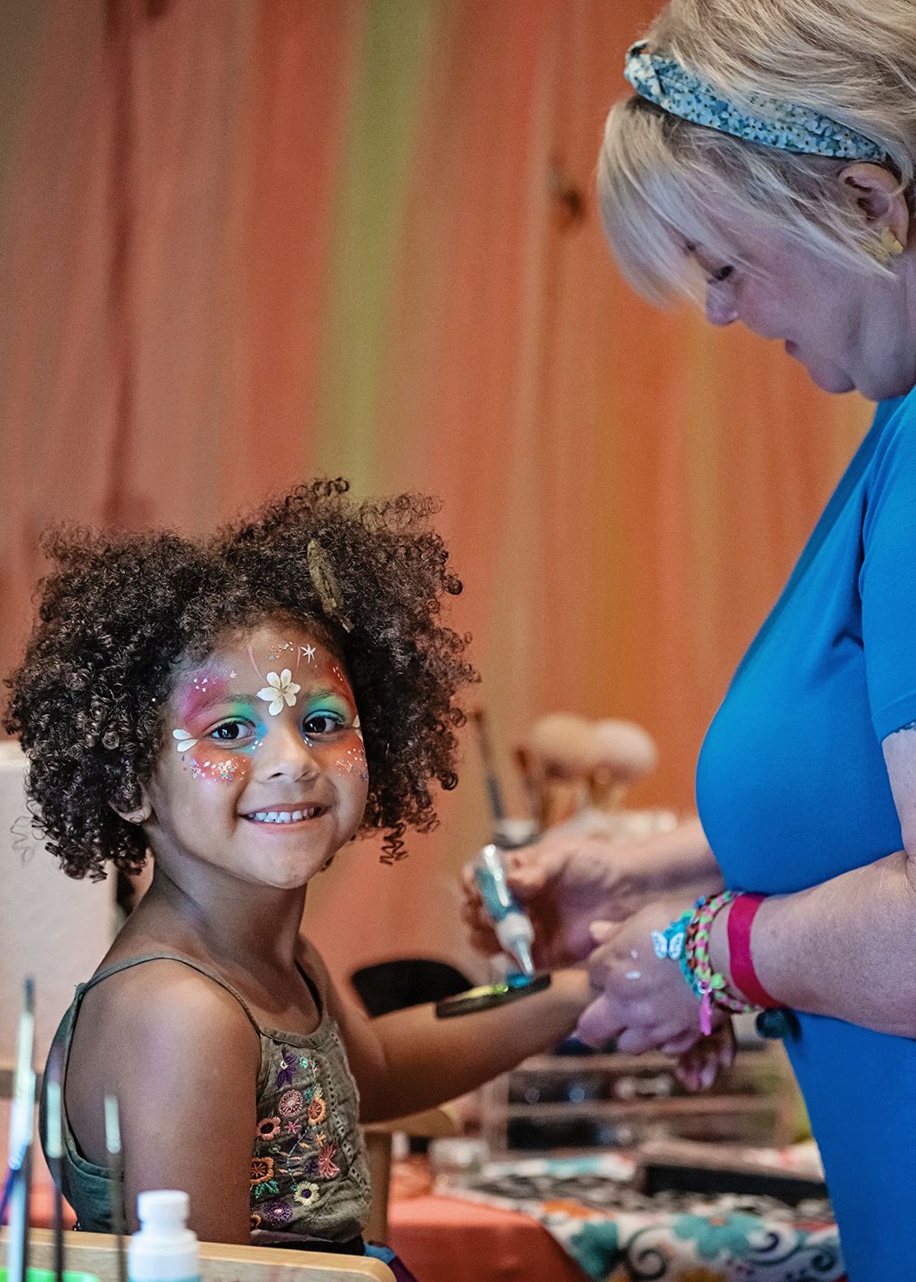 A little girl is getting her face painted by a woman.