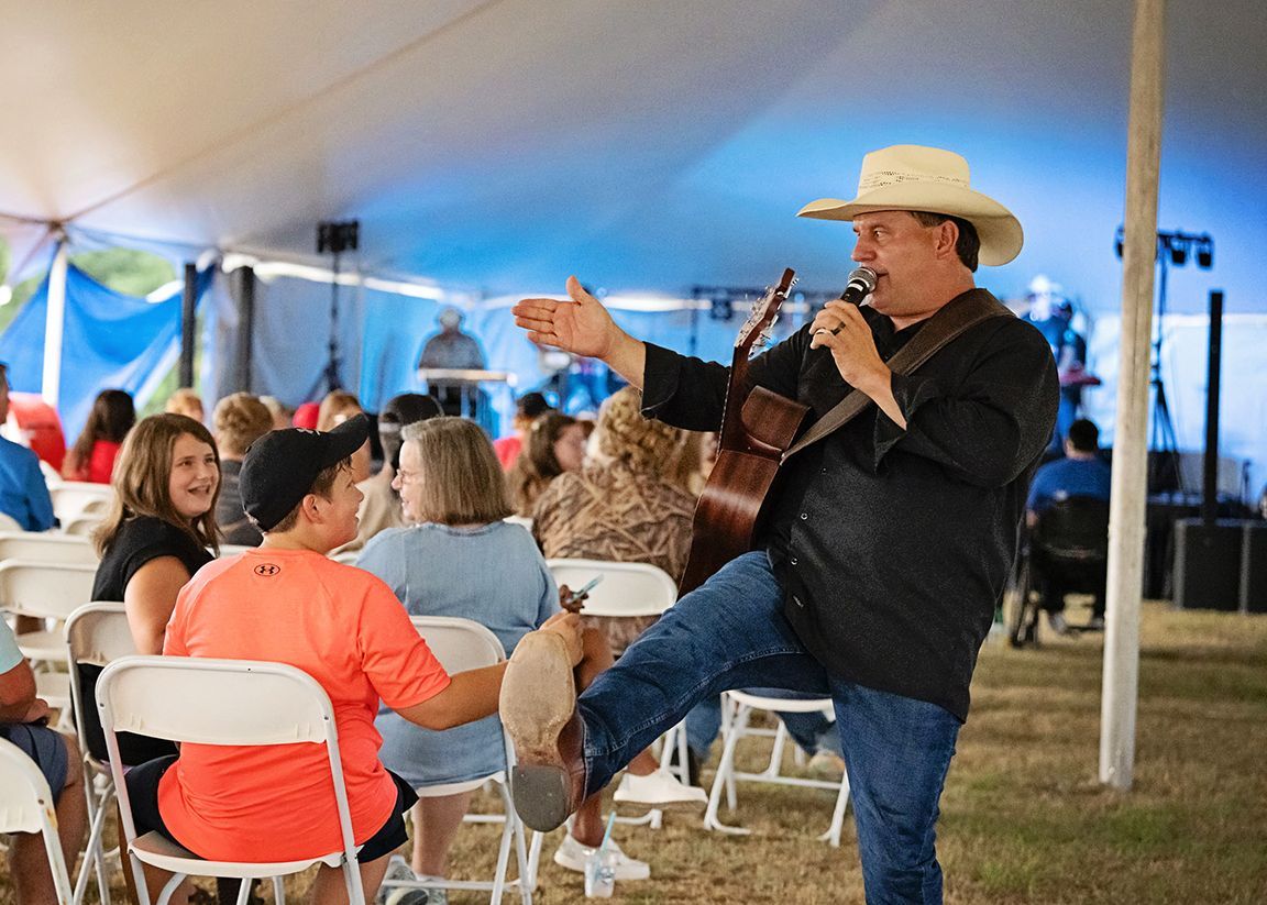 A man in a cowboy hat is playing a guitar and singing into a microphone.