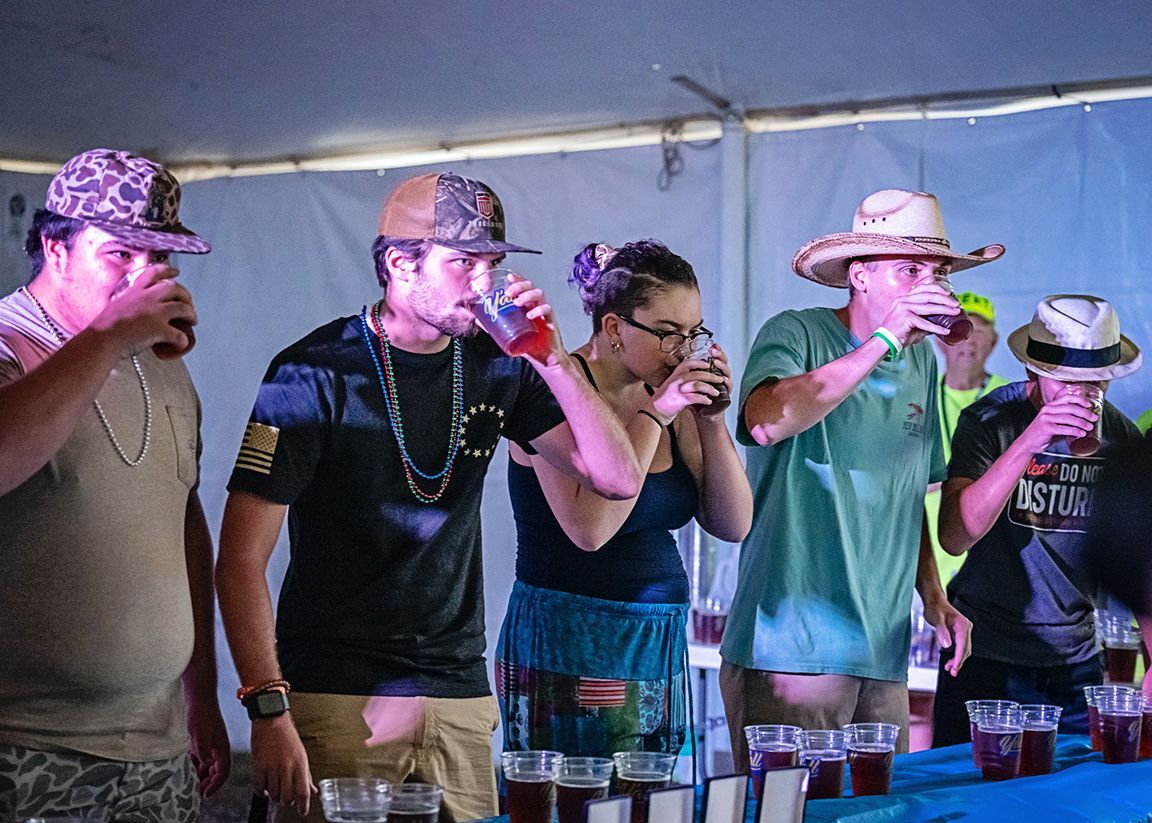 A group of people are standing around a table drinking beer.