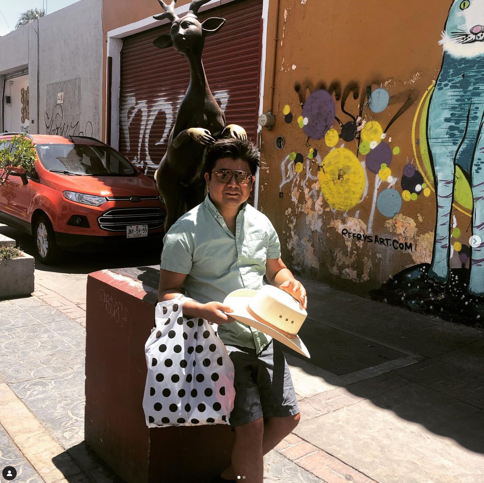 Mario Arellanes of Ryan Levis Architect, Inc., sitting on a bench holding a hat and a polka dot bag