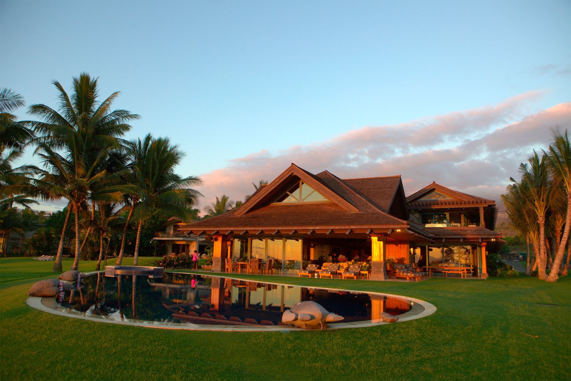 A view of the rear of the Makena Waterfront Estate in Maui, HI, at dusk, with the swimming pool in the foreground.