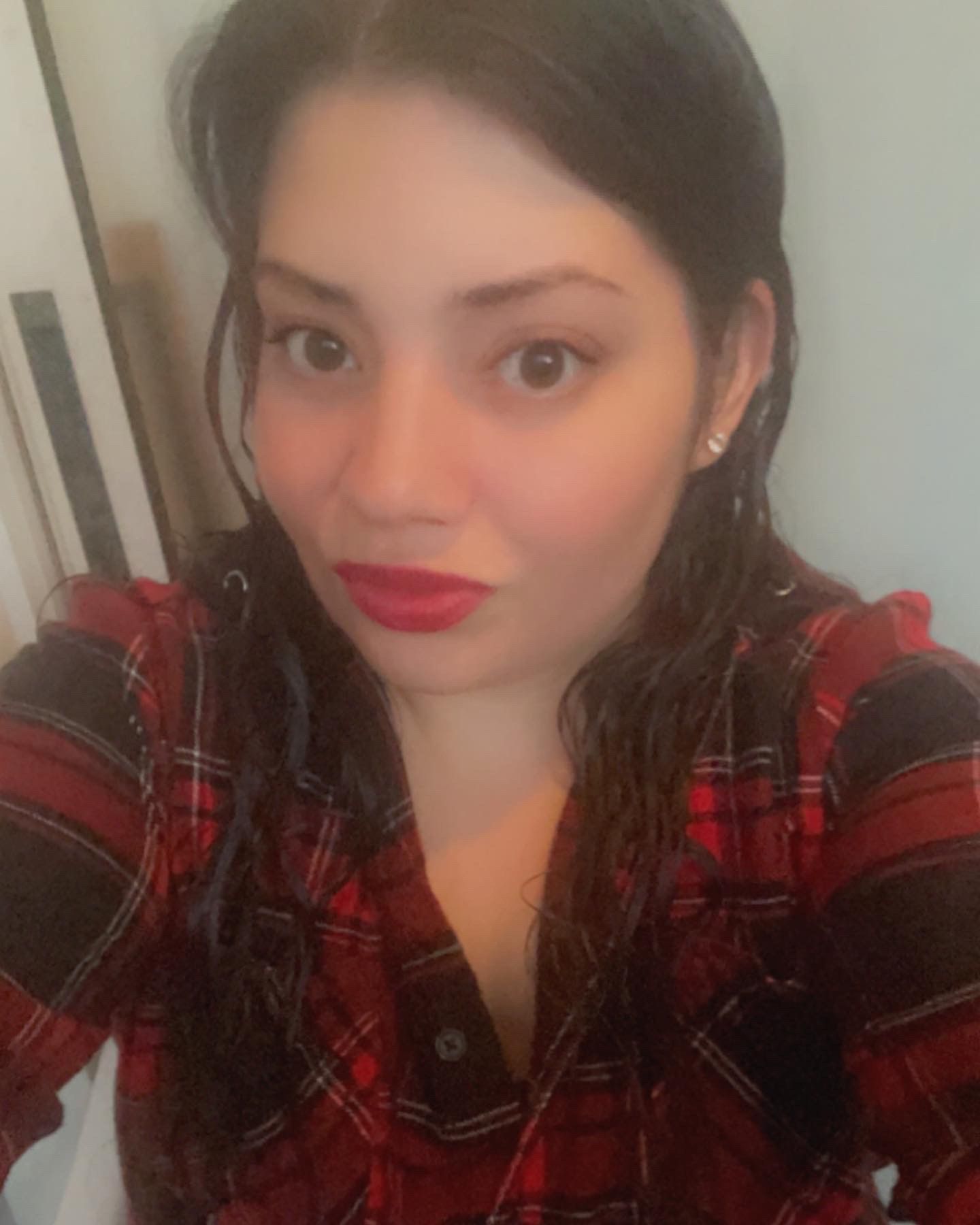 A woman wearing a plaid shirt and red lipstick is taking a selfie.