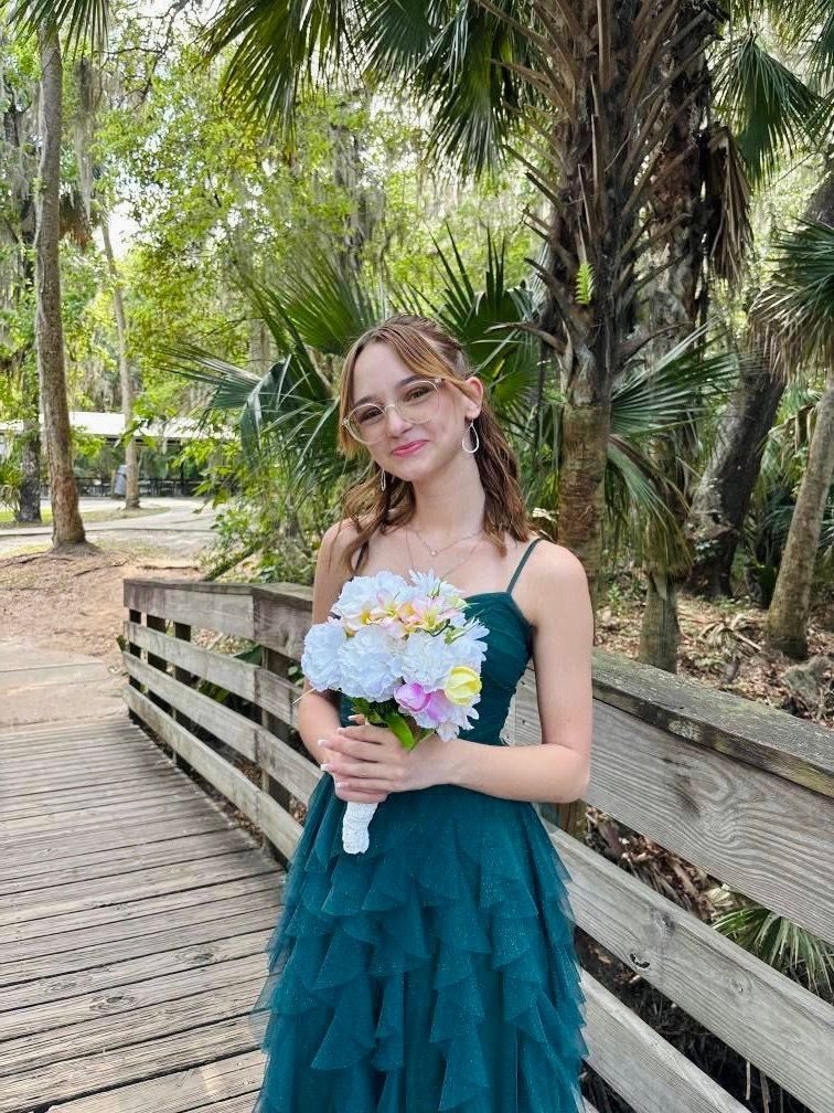 A woman in a green dress is holding a bouquet of flowers on a wooden bridge.