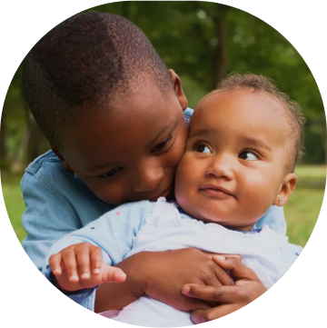 A young boy holds a baby in his arms