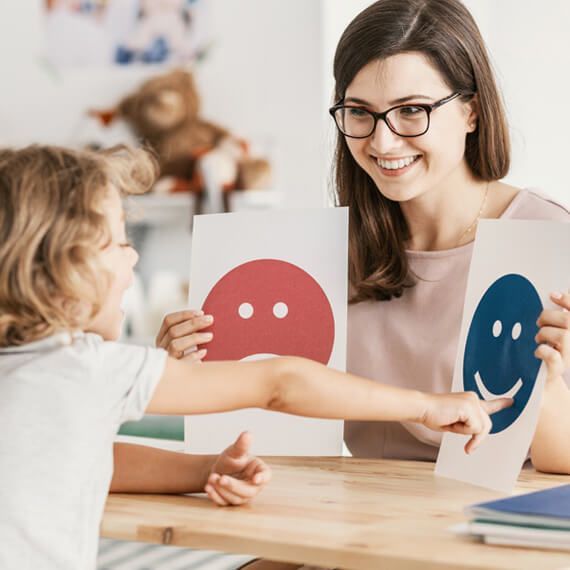 A woman and a child are sitting at a table holding pictures of smiley faces.