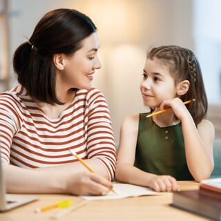 A woman and a little girl are sitting at a table with pencils in their hands.