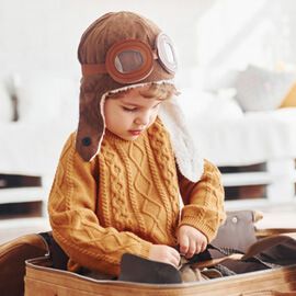 A little boy wearing a pilot 's hat and goggles is playing with a suitcase.