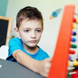 A young boy is playing with a wooden abacus.