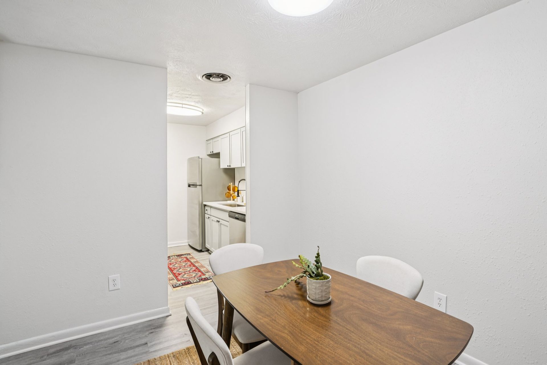 A dining room with a wooden table, three chairs, and a view into a white kitchen.