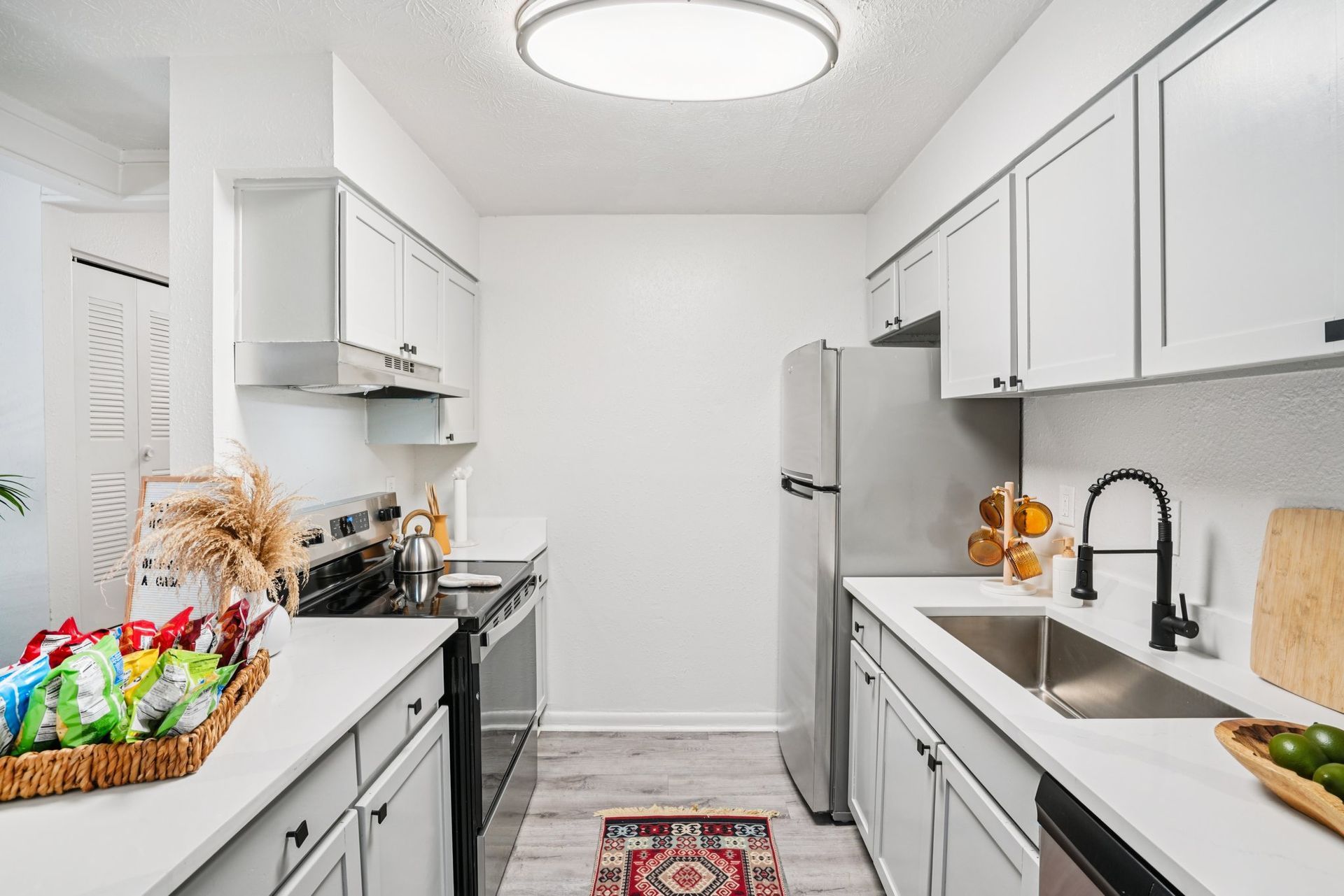 Modern kitchen with white cabinets, stainless steel appliances, and a small rug. Chips and limes are visible.