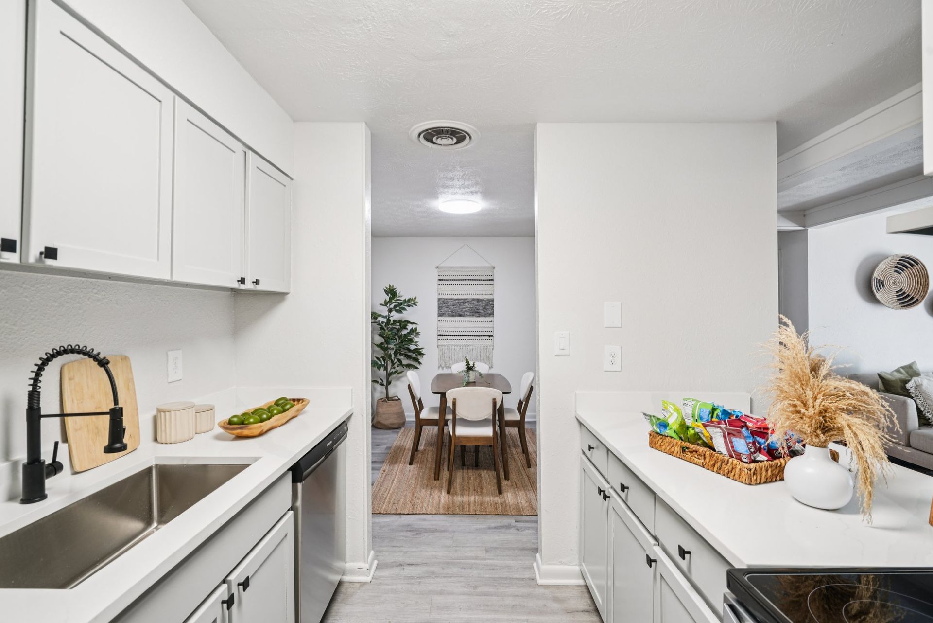 Kitchen with white cabinets, countertop, and appliances, leading to a dining area with a table, chairs, and decorative elements.