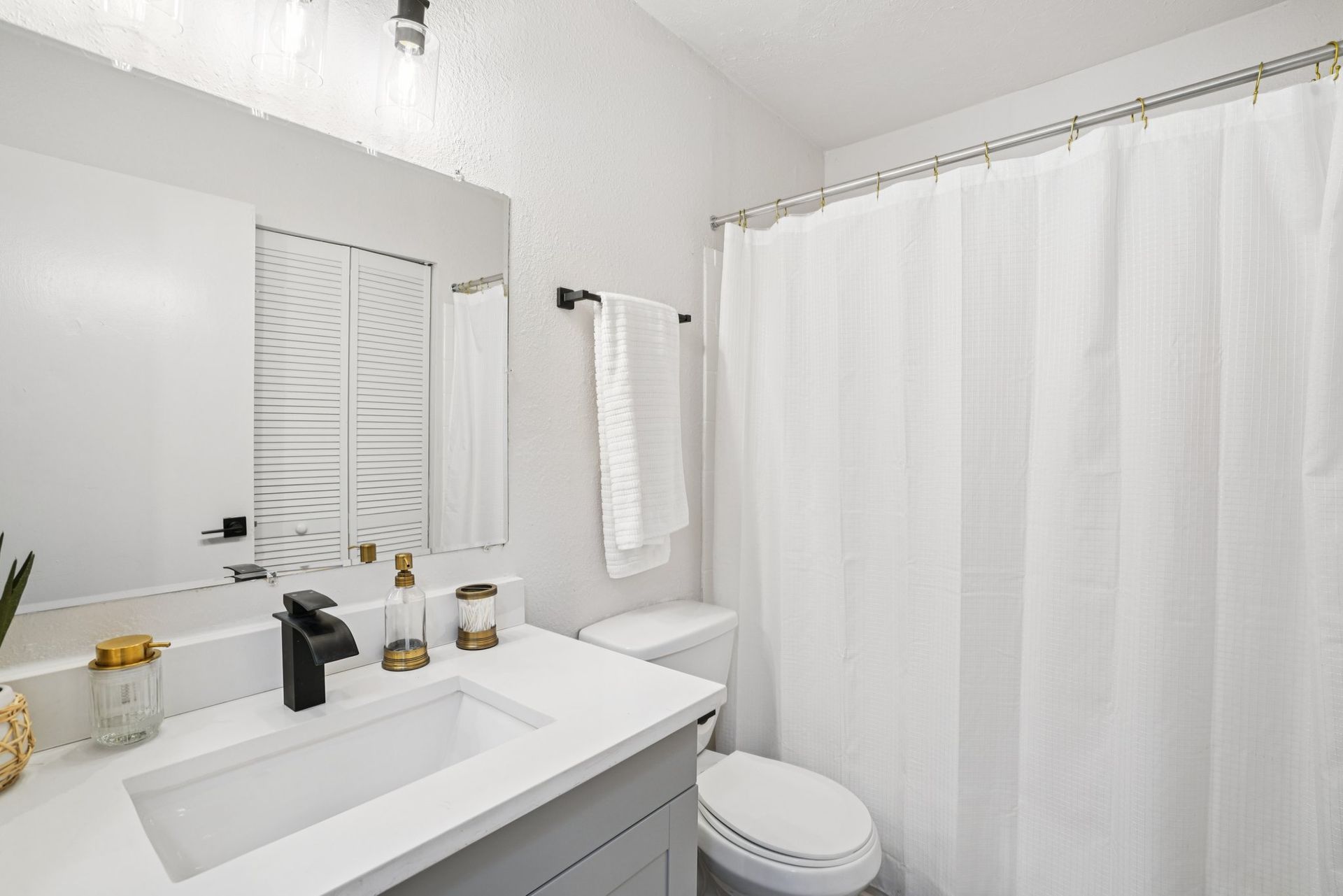 White bathroom with a vanity, toilet, shower curtain, and decor.