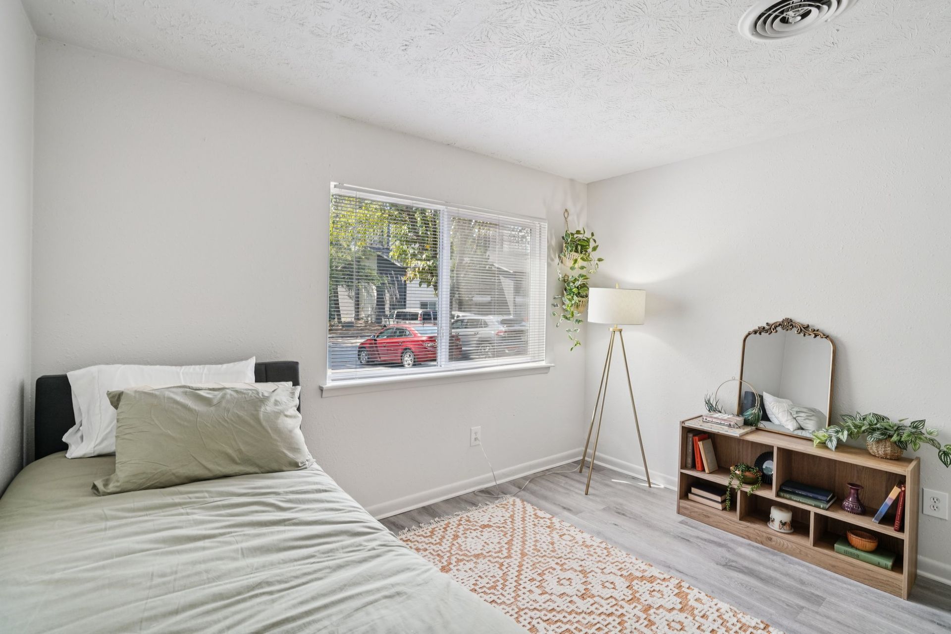 Bedroom with a bed, window, bookshelf, and floor lamp. Soft colors and natural light create a bright, inviting space.