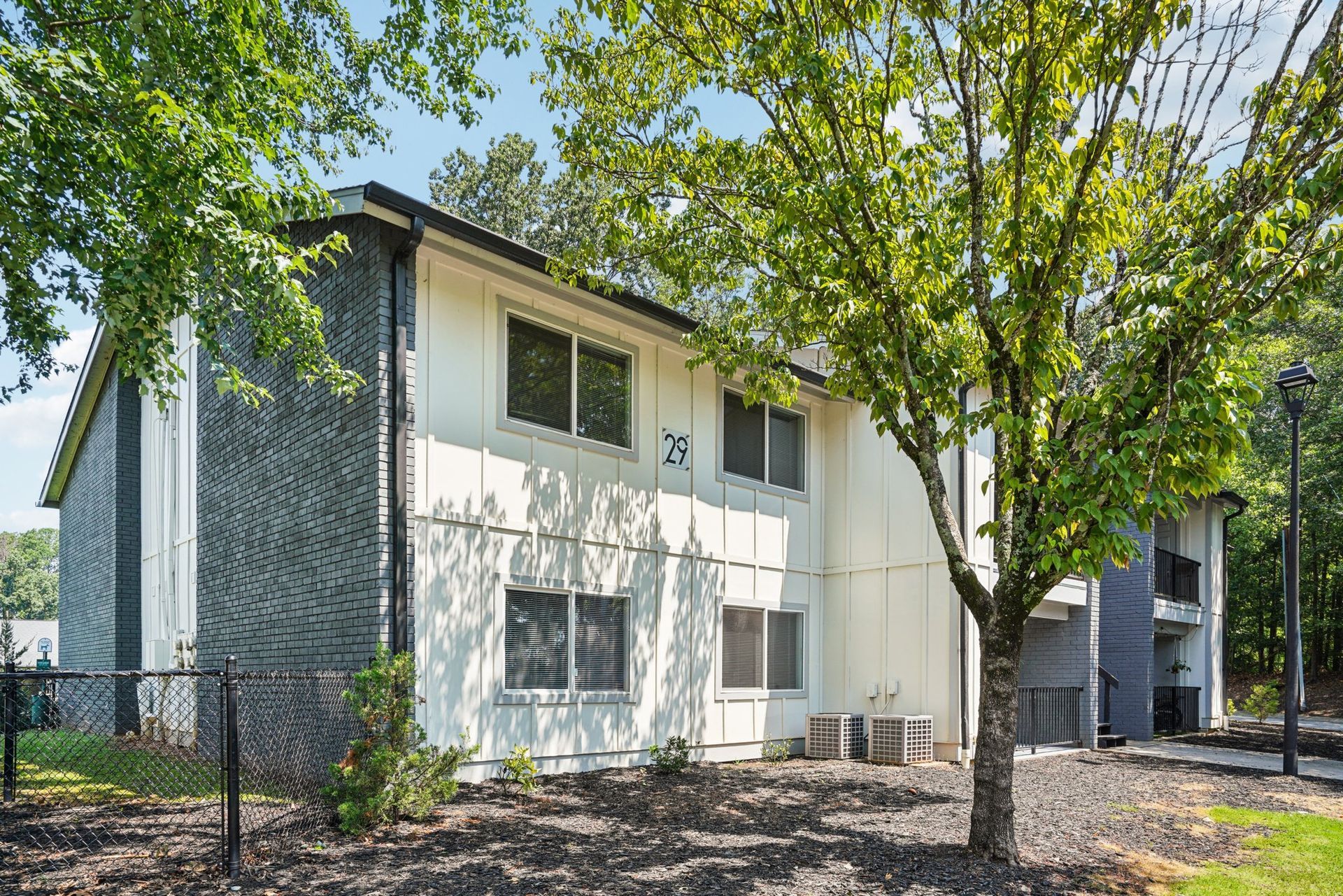 Two-story apartment building with white and gray siding, surrounded by trees and a fence. Building number 75 is visible.