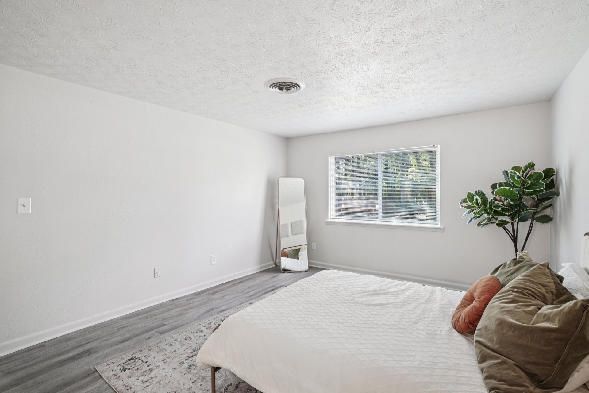 A bright bedroom with a bed, closet, and a doorway leading to a bathroom, all in white and light wood tones.