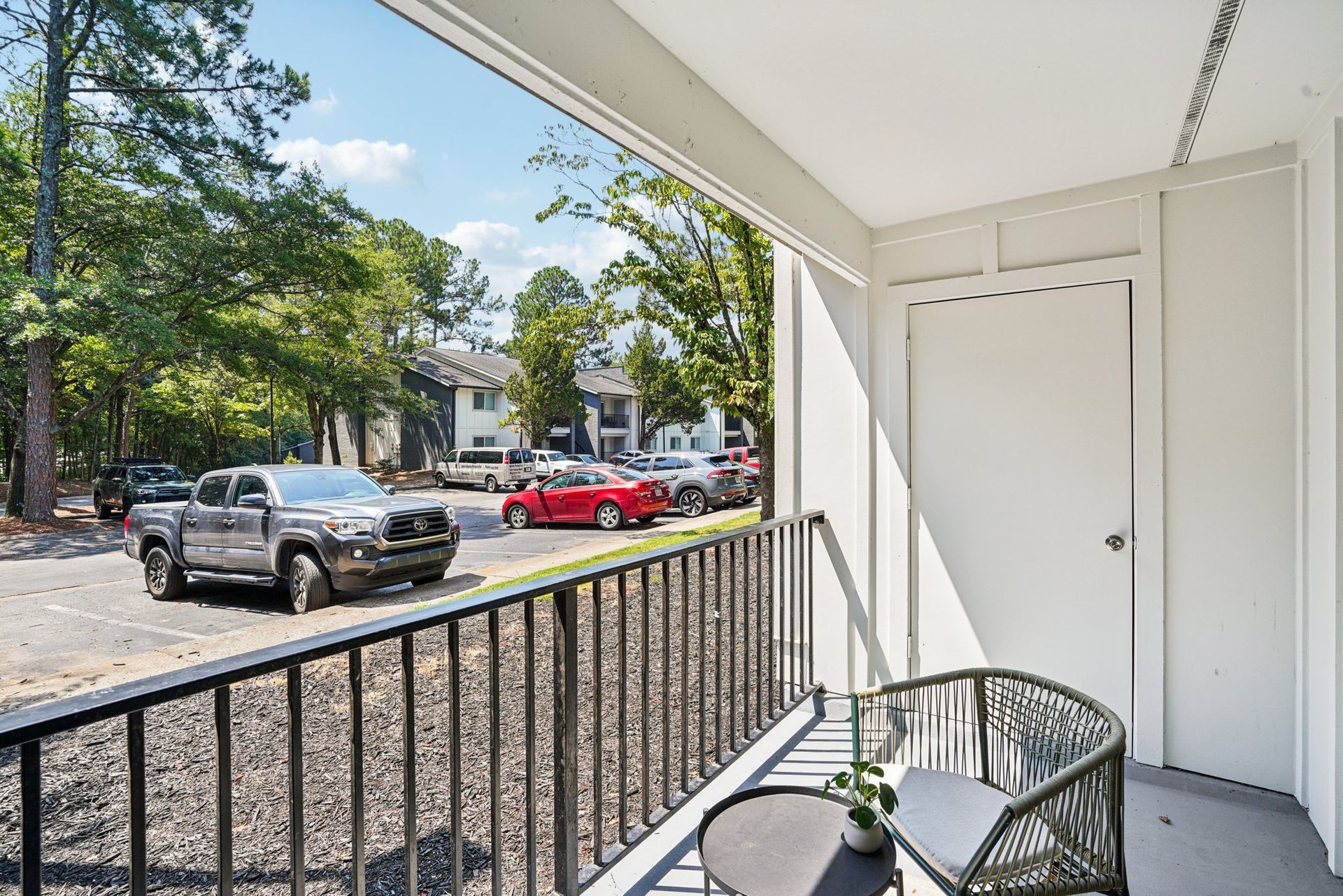 View from a balcony of a parking lot with cars and apartment buildings. The balcony has a small table and chairs.