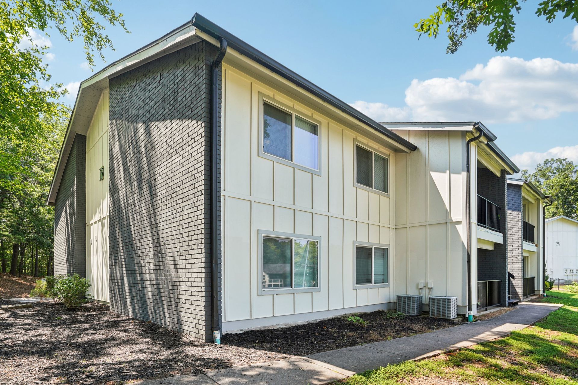 Two-story apartment building with light-colored siding, black trim, and windows; set in a grassy area with trees.