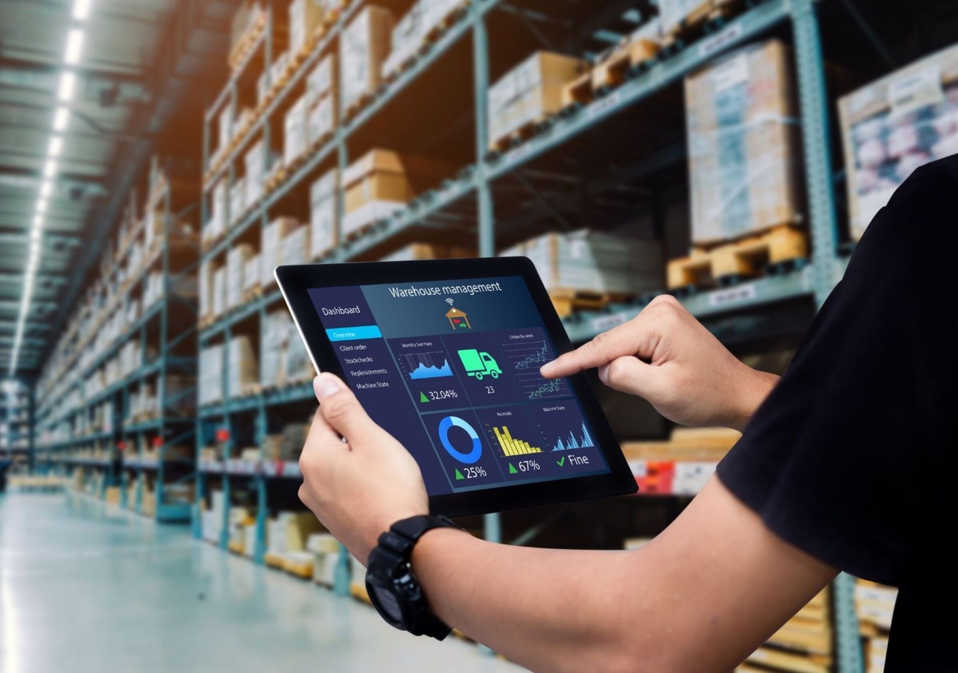 Person uses a tablet in a warehouse, viewing data analytics; boxes on shelves in background.