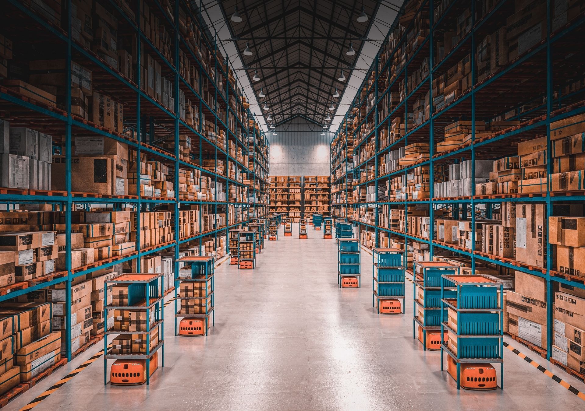 Warehouse interior with rows of shelves filled with boxes, robots moving items, and a concrete floor.