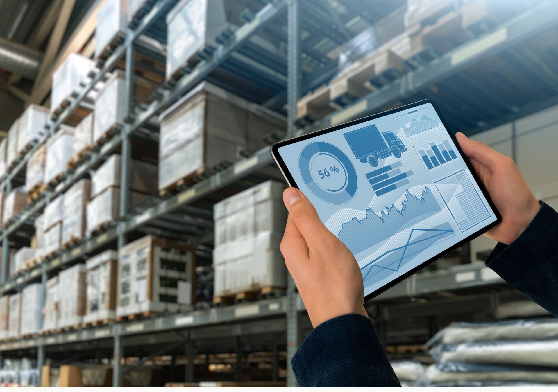 Person holding tablet with warehouse inventory data, shelves of boxes in background.