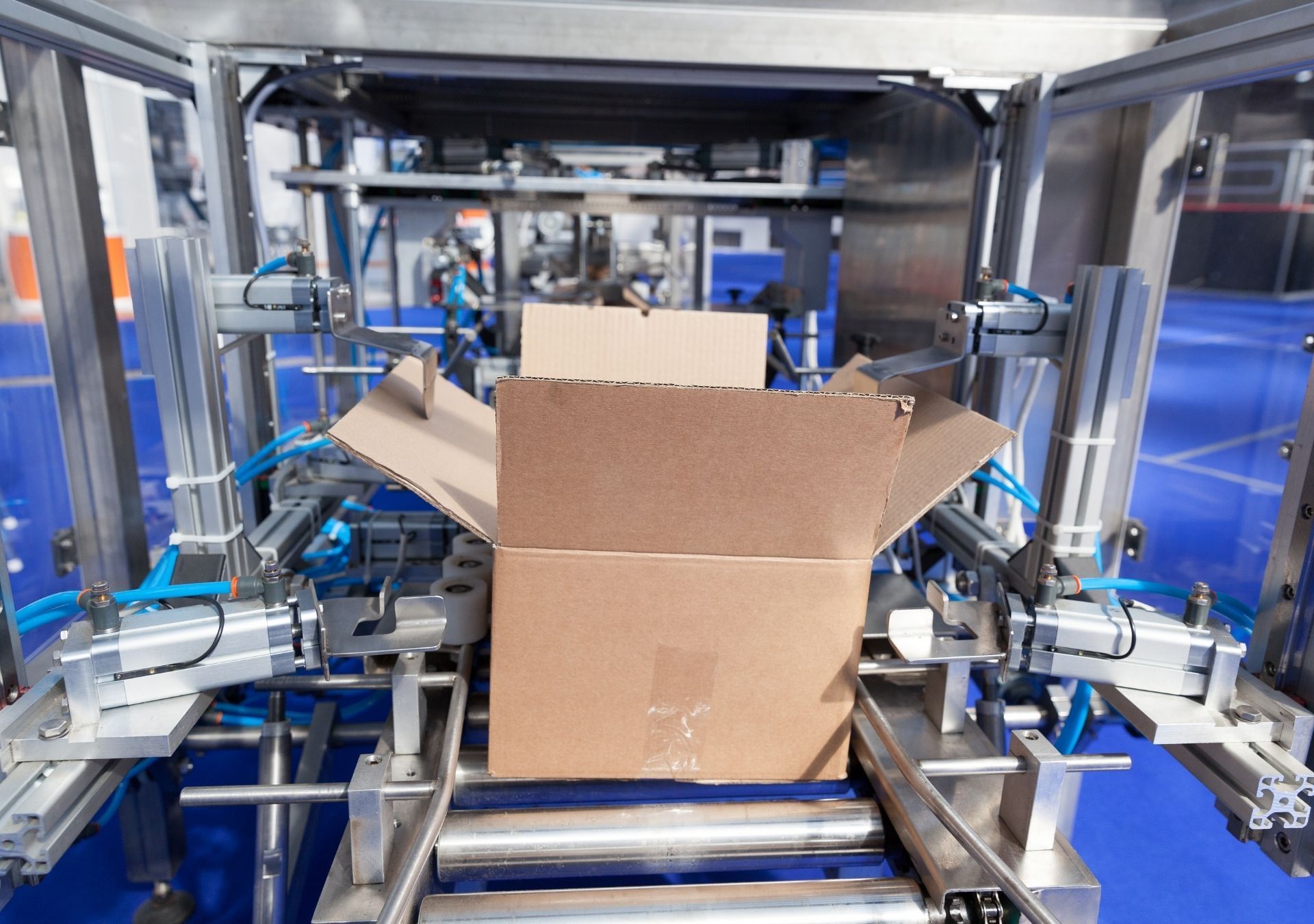 Automated machine opening a cardboard box on a conveyor belt in a factory.
