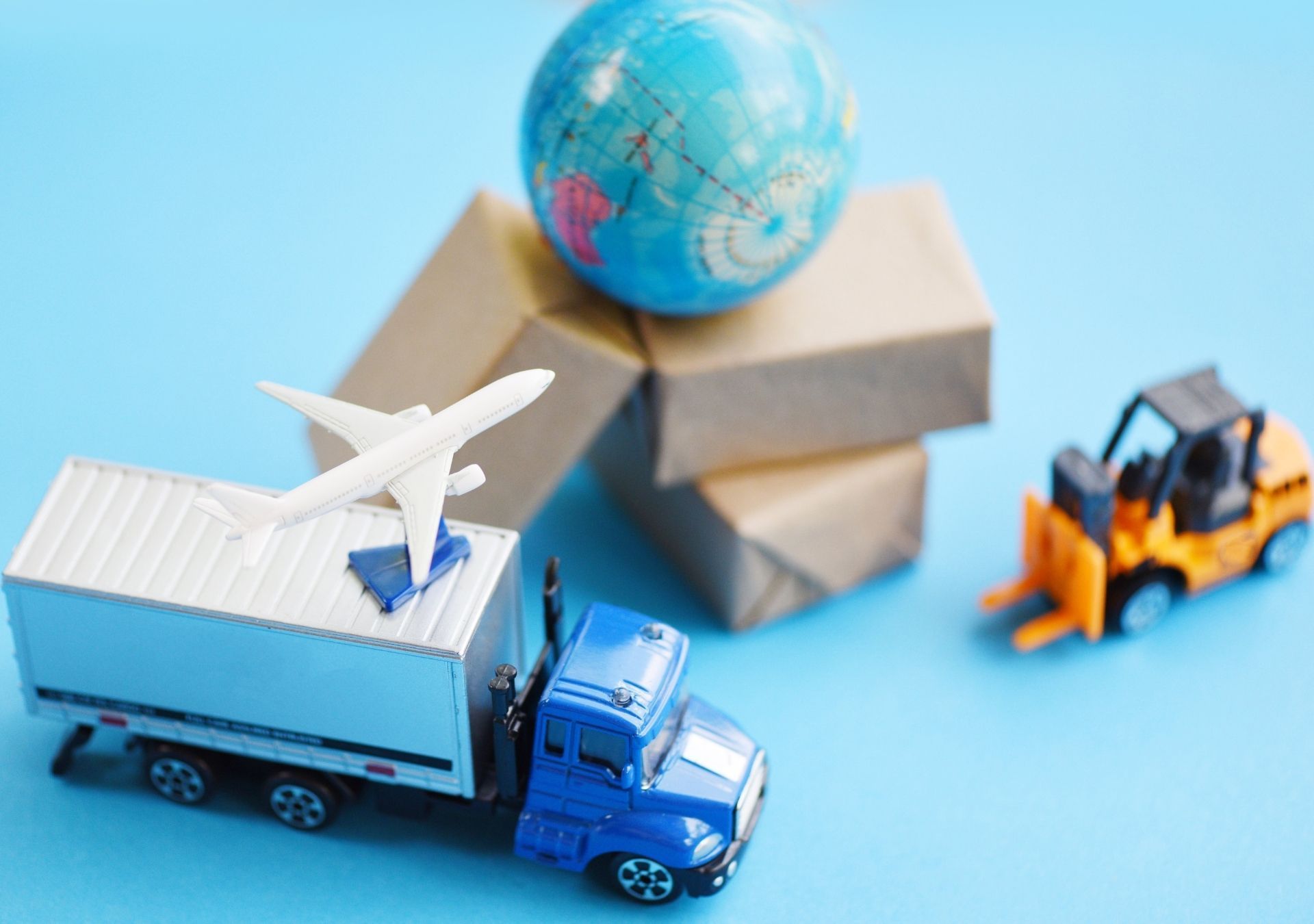 Toy truck, airplane, and forklift with stacked packages and globe, illustrating global shipping.