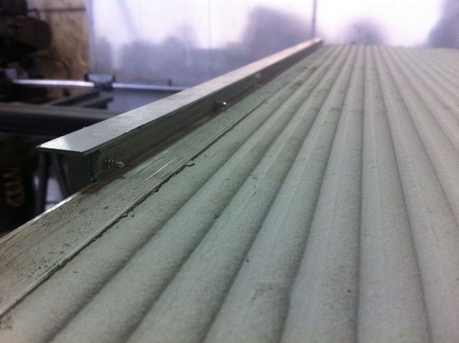 Un elemento di finitura metallico installato sul bordo di una superficie scanalata di colore chiaro.