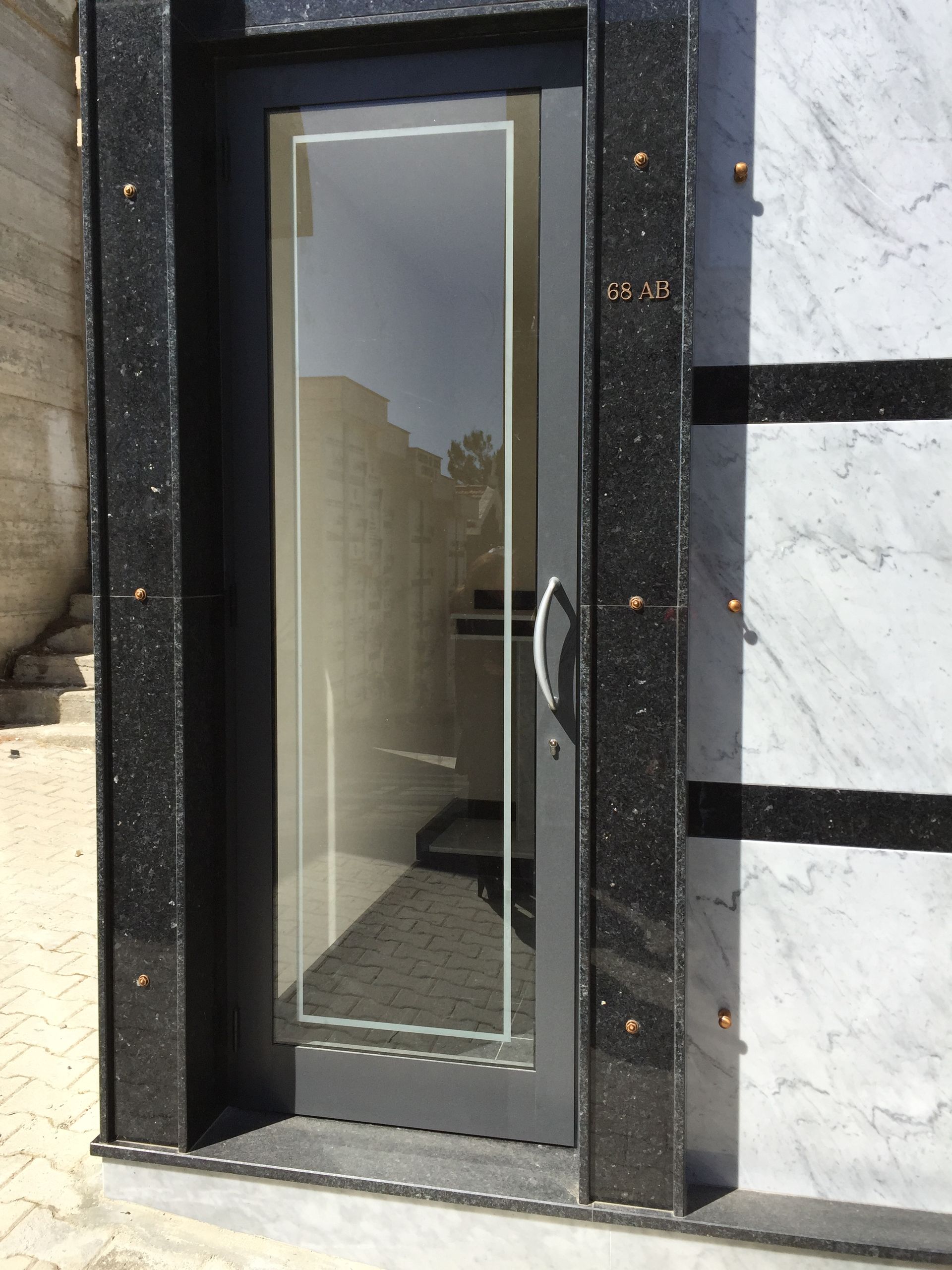 Una porta a vetri incastonata in una cornice di granito nero accanto a una parete rivestita di pannelli di marmo bianco e nero.