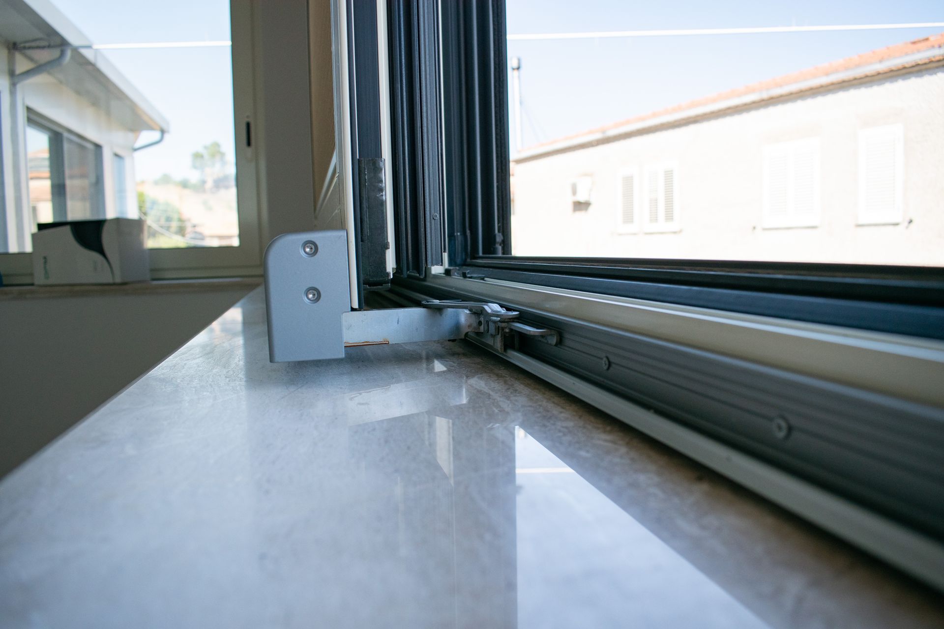 Primo piano di un davanzale che mostra una staffa per persiana grigia installata su una mensola di pietra chiara e lucida.