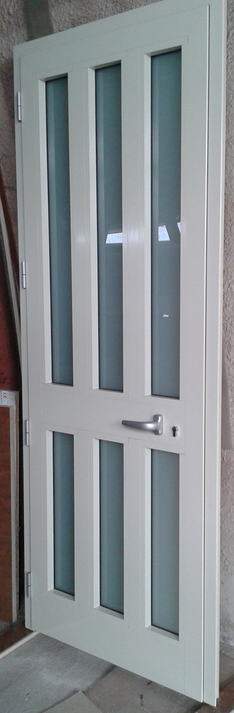 Una porta interna singola bianca con sei pannelli verticali in vetro satinato e maniglia argentata, mostrata addossata a una parete.