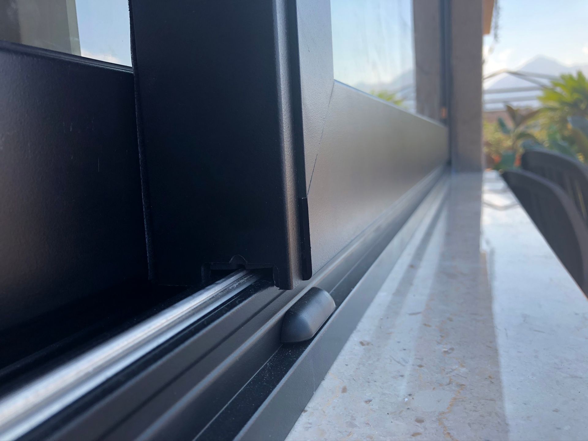 Primo piano del telaio e del binario in metallo nero di una porta scorrevole in vetro, sullo sfondo di un davanzale in marmo.