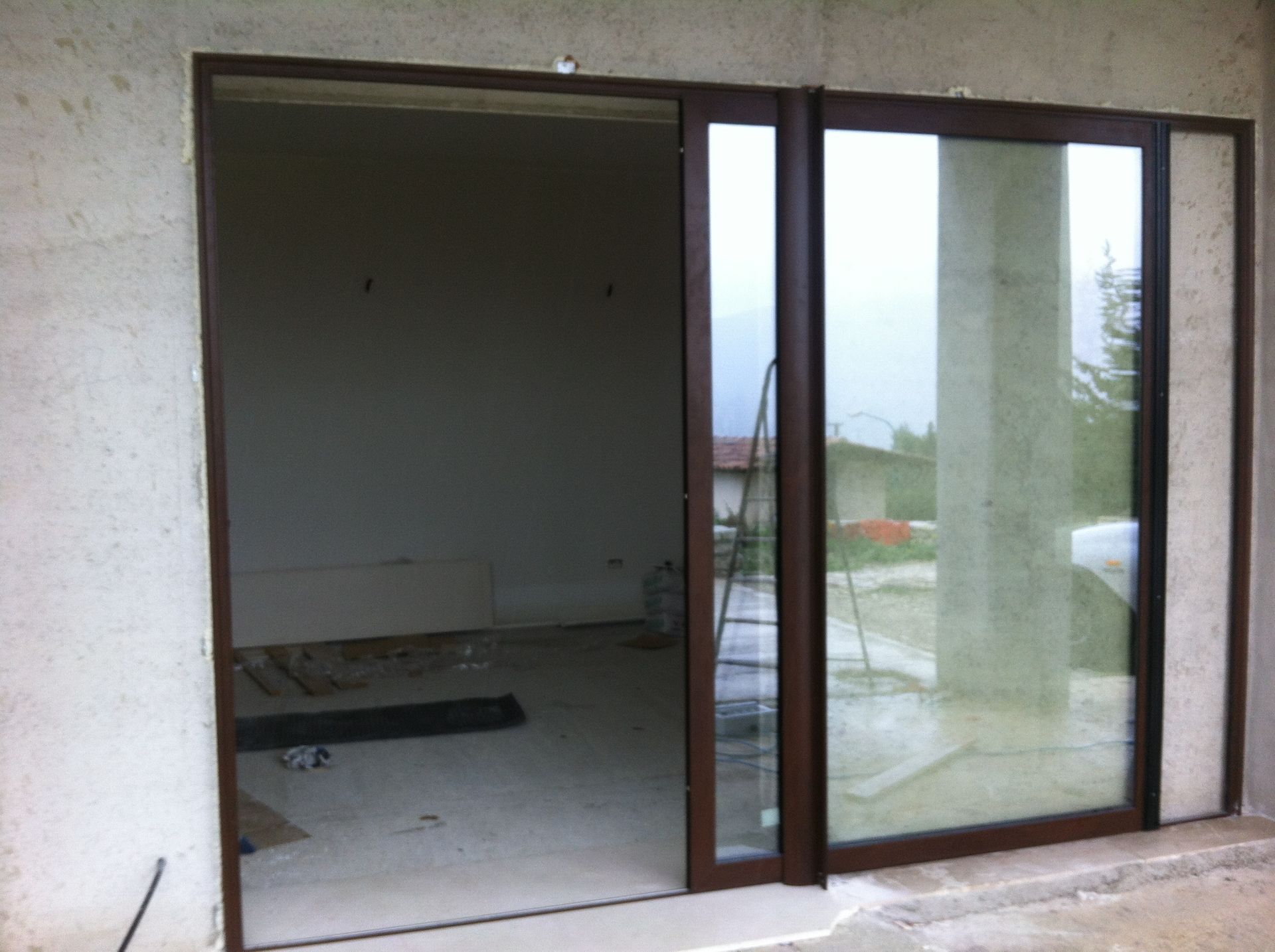 Una porta scorrevole in vetro con cornice marrone è parzialmente aperta, rivelando una stanza non rifinita con pavimento in cemento e pareti spoglie.