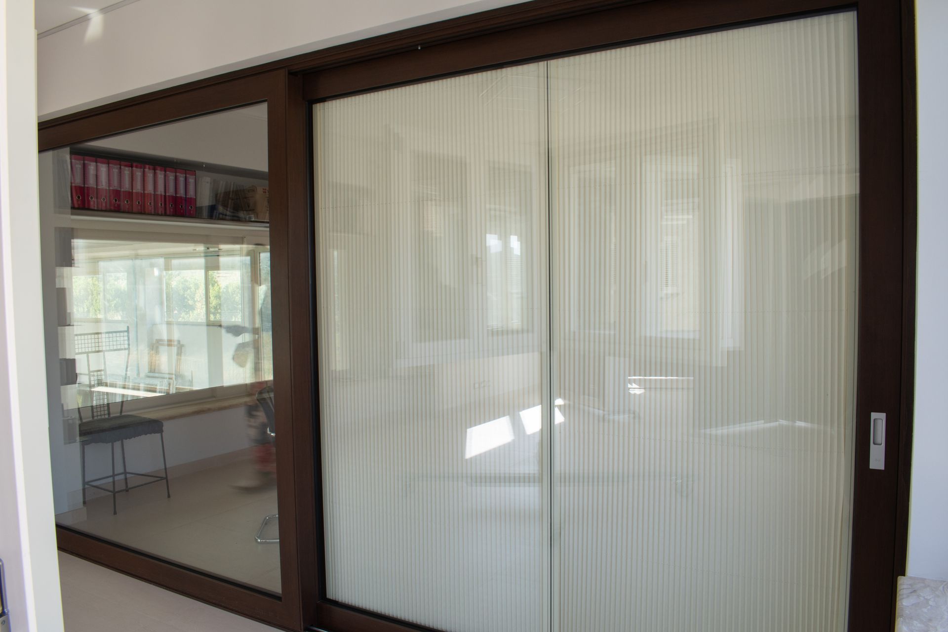 Una parete di finestre e porte scorrevoli in vetro con tende verticali in un luminoso e moderno spazio ufficio interno.