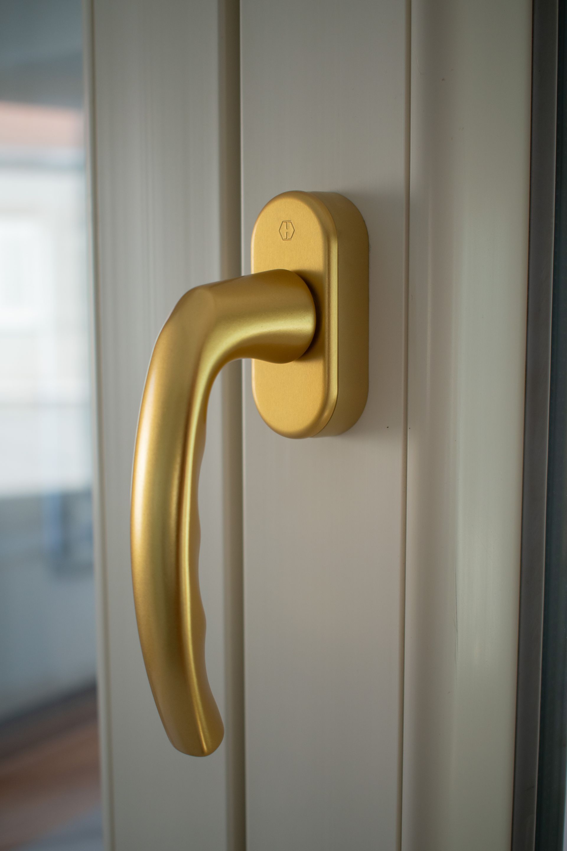 Maniglia per porta in metallo color oro opaco, montata verticalmente su una cornice bianca.