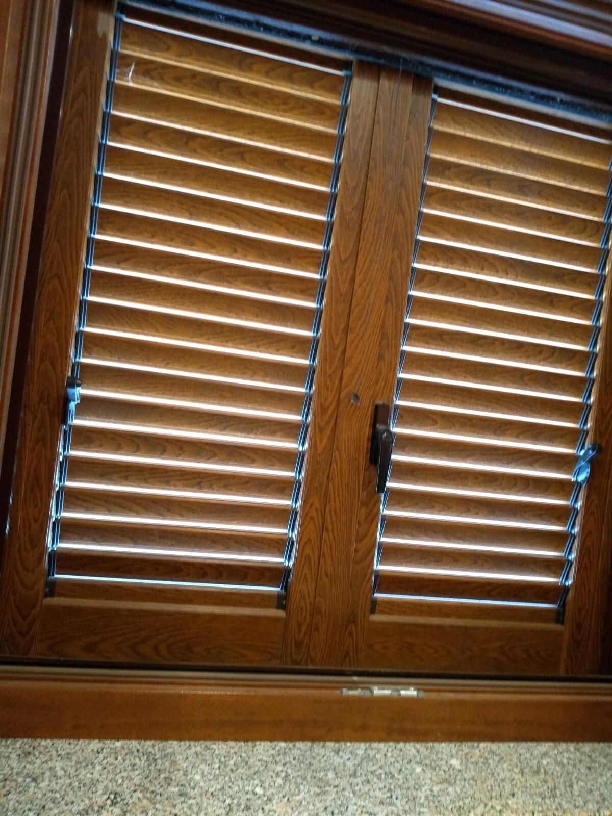 Persiane chiuse con lamelle orizzontali in legno di tonalità media, installate su porte a doppio battente.