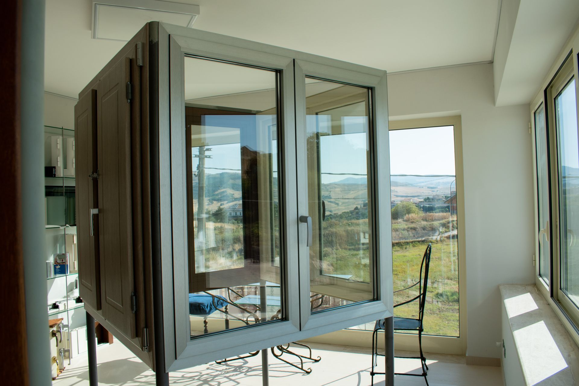 Una vetrina a doppio vetro argentata è posizionata su una struttura metallica all'interno di una stanza soleggiata con ampie finestre che si affacciano su una valle.