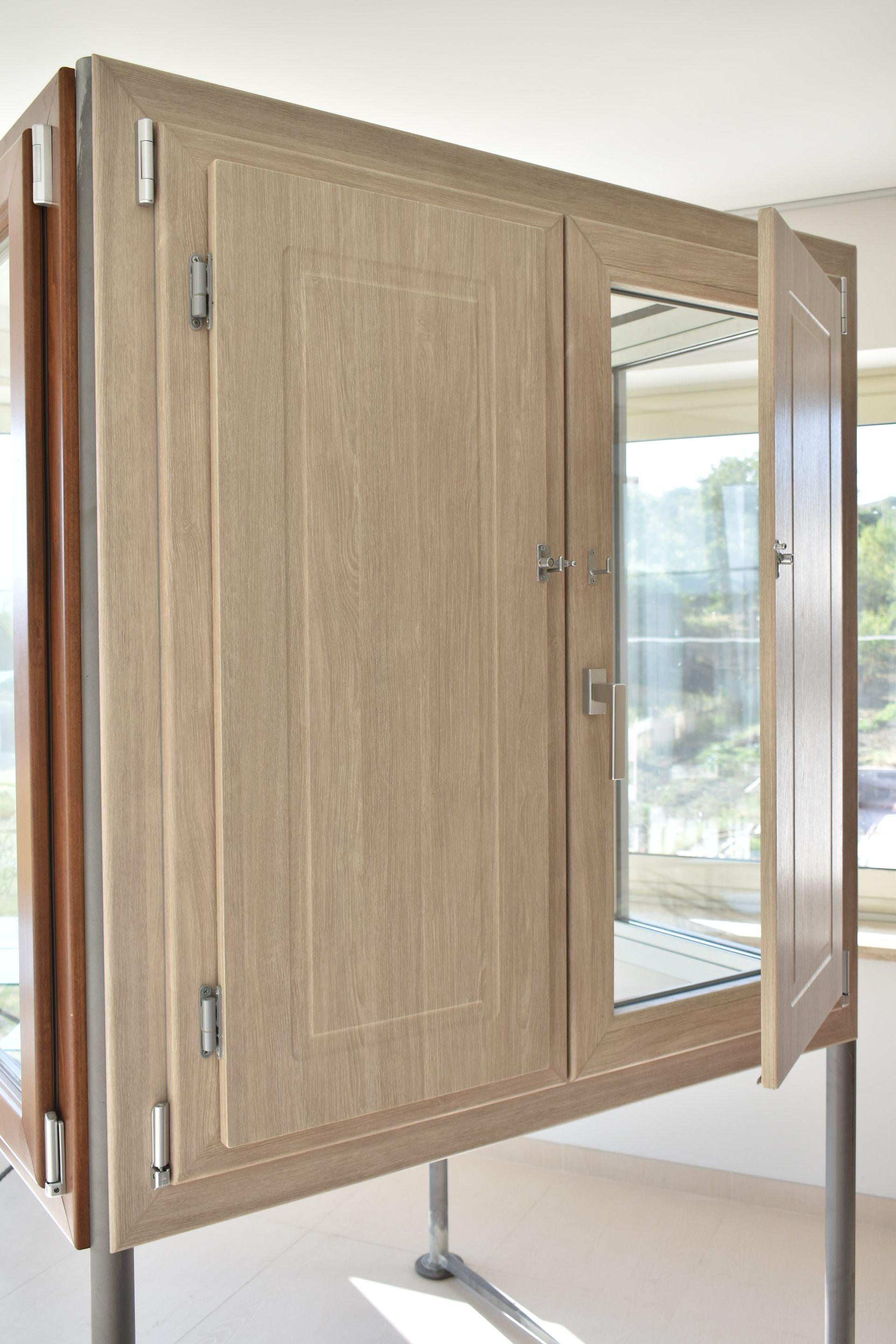 Un telaio di finestra in legno chiaro con pannelli di vetro poggiati su supporti metallici, che mostra un lato parzialmente aperto.