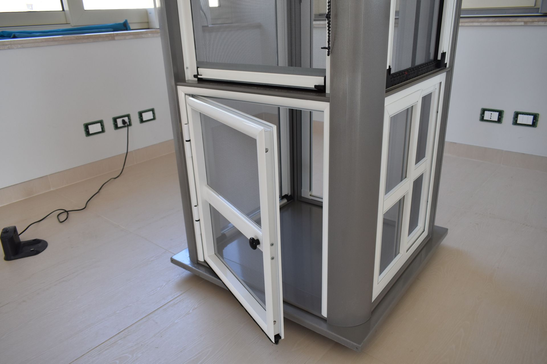 Un mobile espositivo da terra, bianco e grigio, con una piccola anta, posizionato su un pavimento chiaro in una stanza.