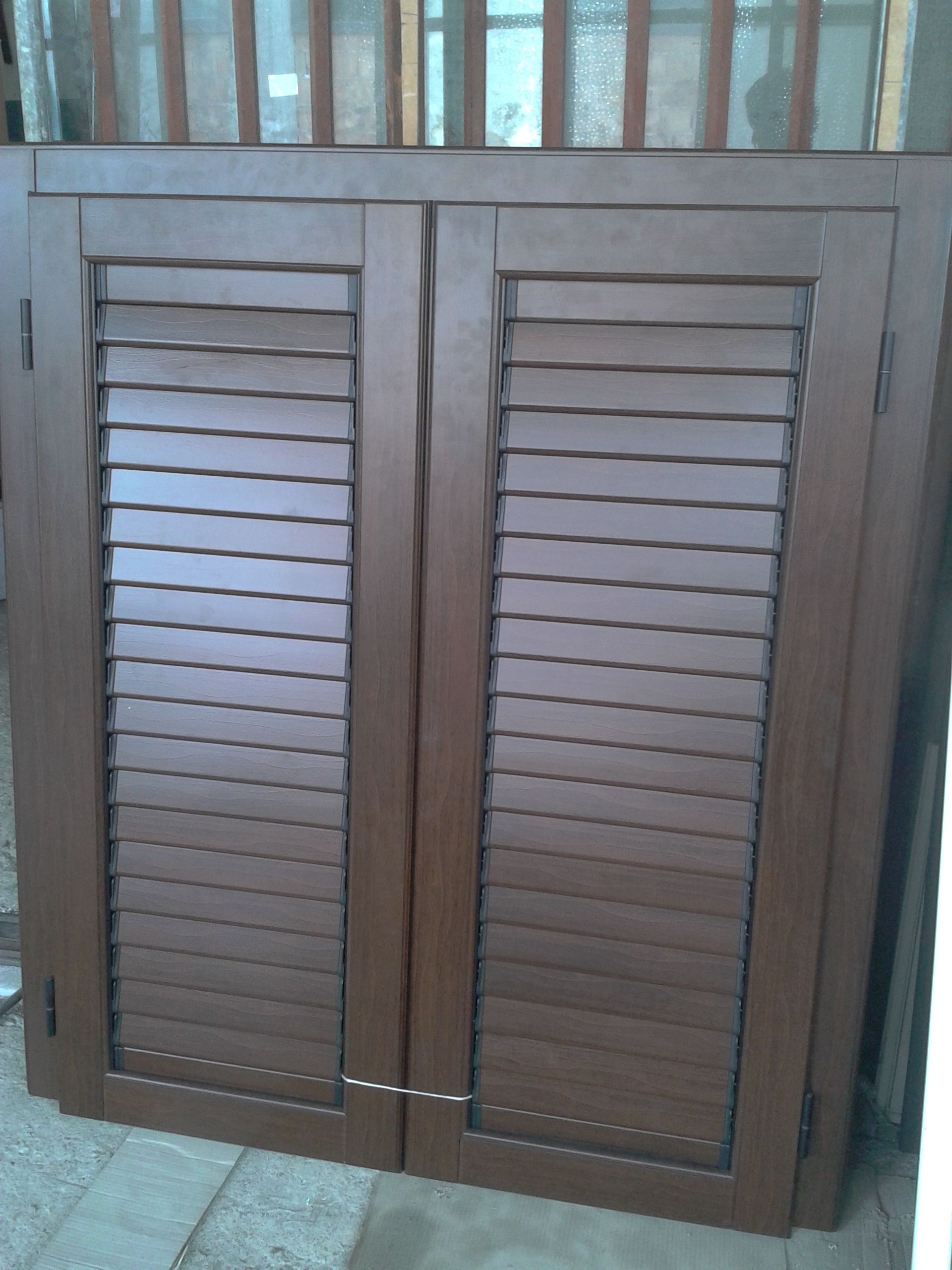 Una coppia di persiane in legno marrone chiuse, con lamelle orizzontali, stagliate su uno sfondo chiaro.