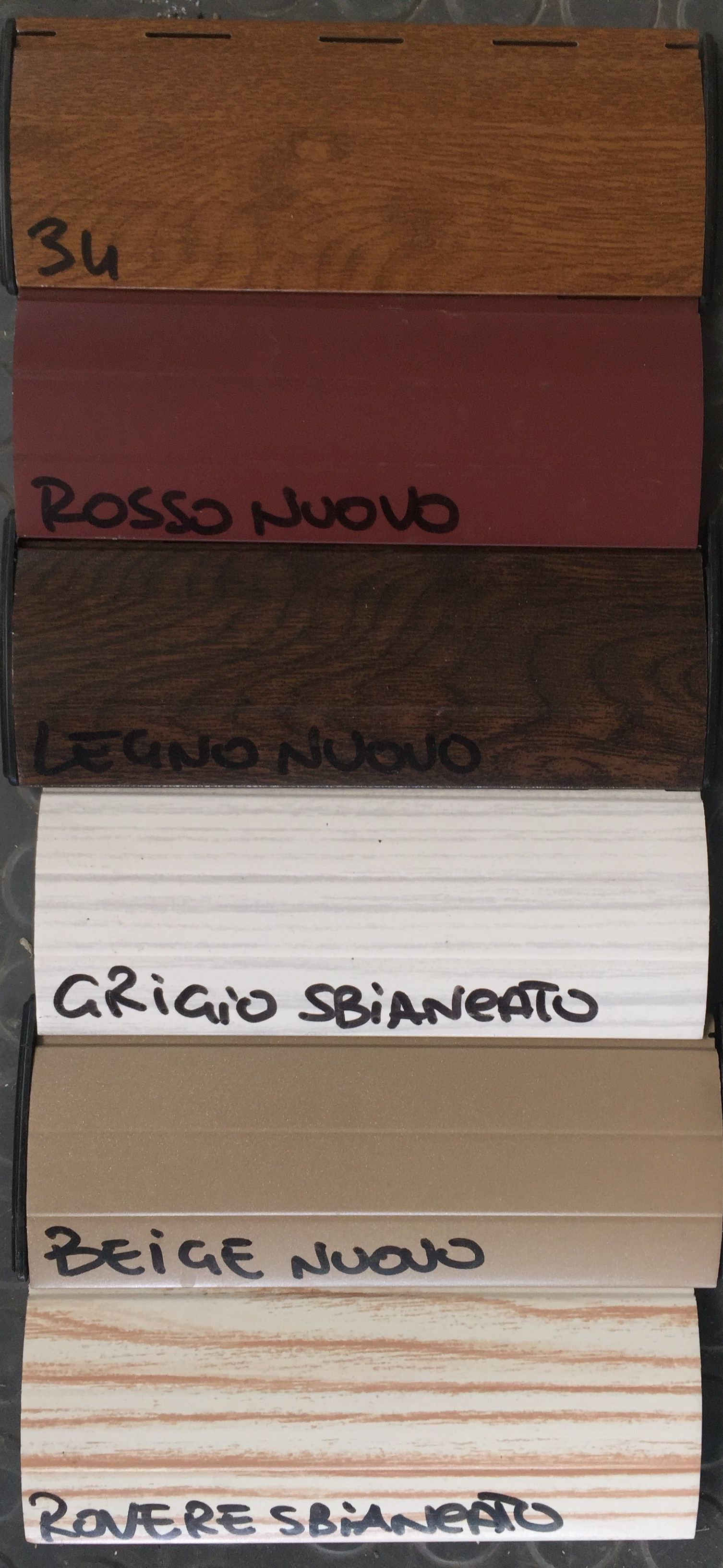 Una pila verticale di sei campioni di finitura per legno, etichettati con i rispettivi nomi: 34, Rosso Nuovo, Legno Nuovo e altri.